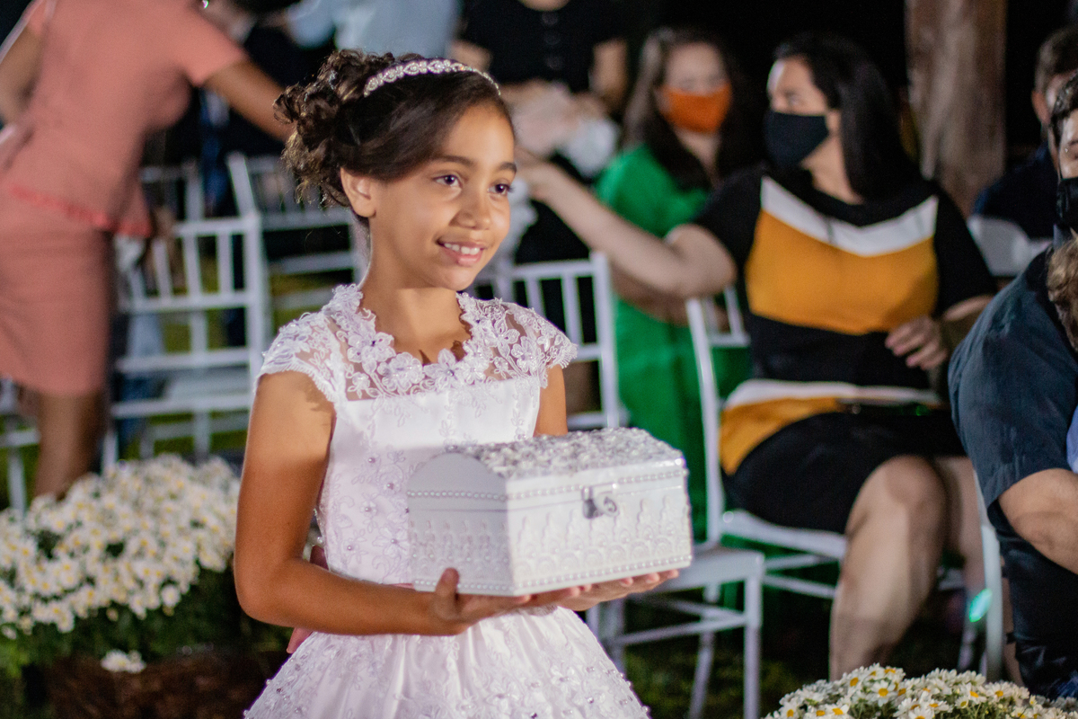 Dama de honra com caixa com véu para a noiva entrando durante cerimônia de casamento durante a festa em Santo Antônio de Pádua interior do Rio de Janeiro. Noiva com buquê em tons de rosa e noivo de terno azul escuro.