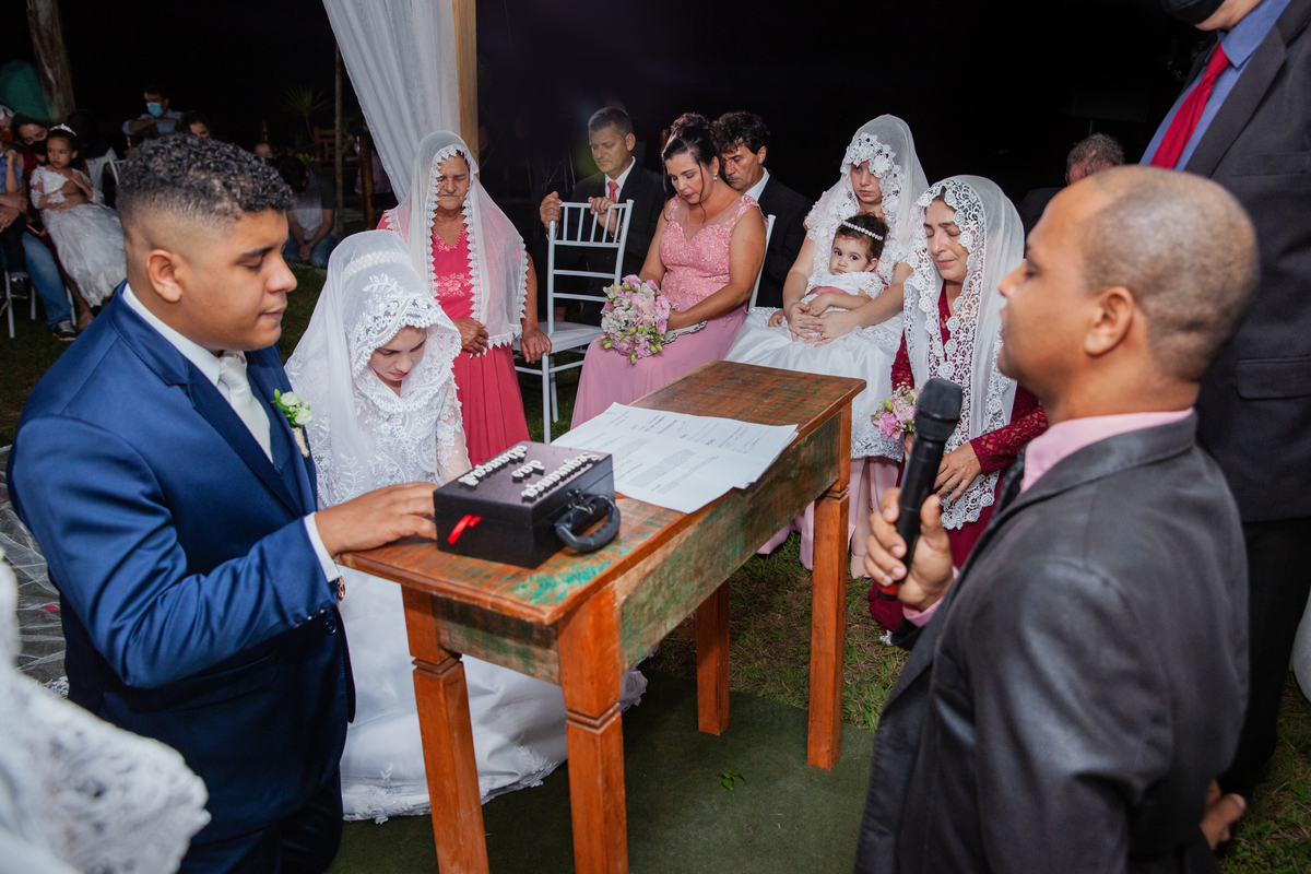 Noivos chorando durante oração no casamento casamento ao ar livre. Noivo com terno azul escuro e noiva com vestido com flores em 3D e véu na cabeça em Santo Antônio de Pádua interior do Rio de Janeiro.