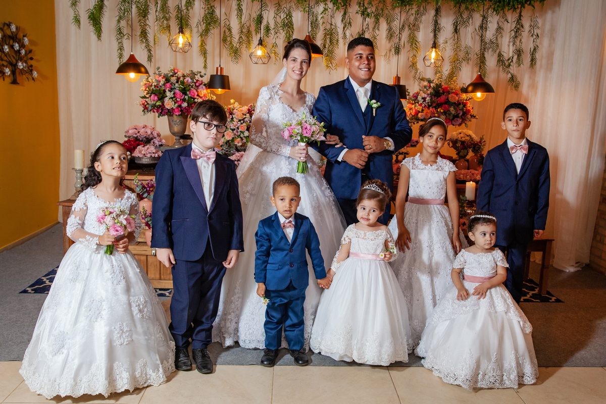 Noivos e daminhas  fazendo fotos na mesa da decoração durante festa de casamento em Santo Antônio de Pádua interior do Rio de Janeiro. Noivos e pajens com terno azul escuro.