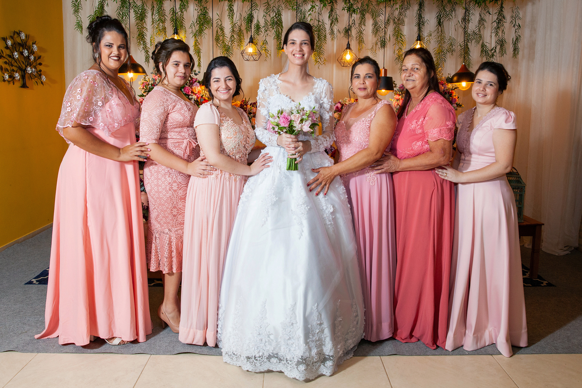 Noiva e Madrinhas em vestidos em tons de rosa fazendo fotos na mesa da decoração durante festa de casamento em Santo Antônio de Pádua interior do Rio de Janeiro.