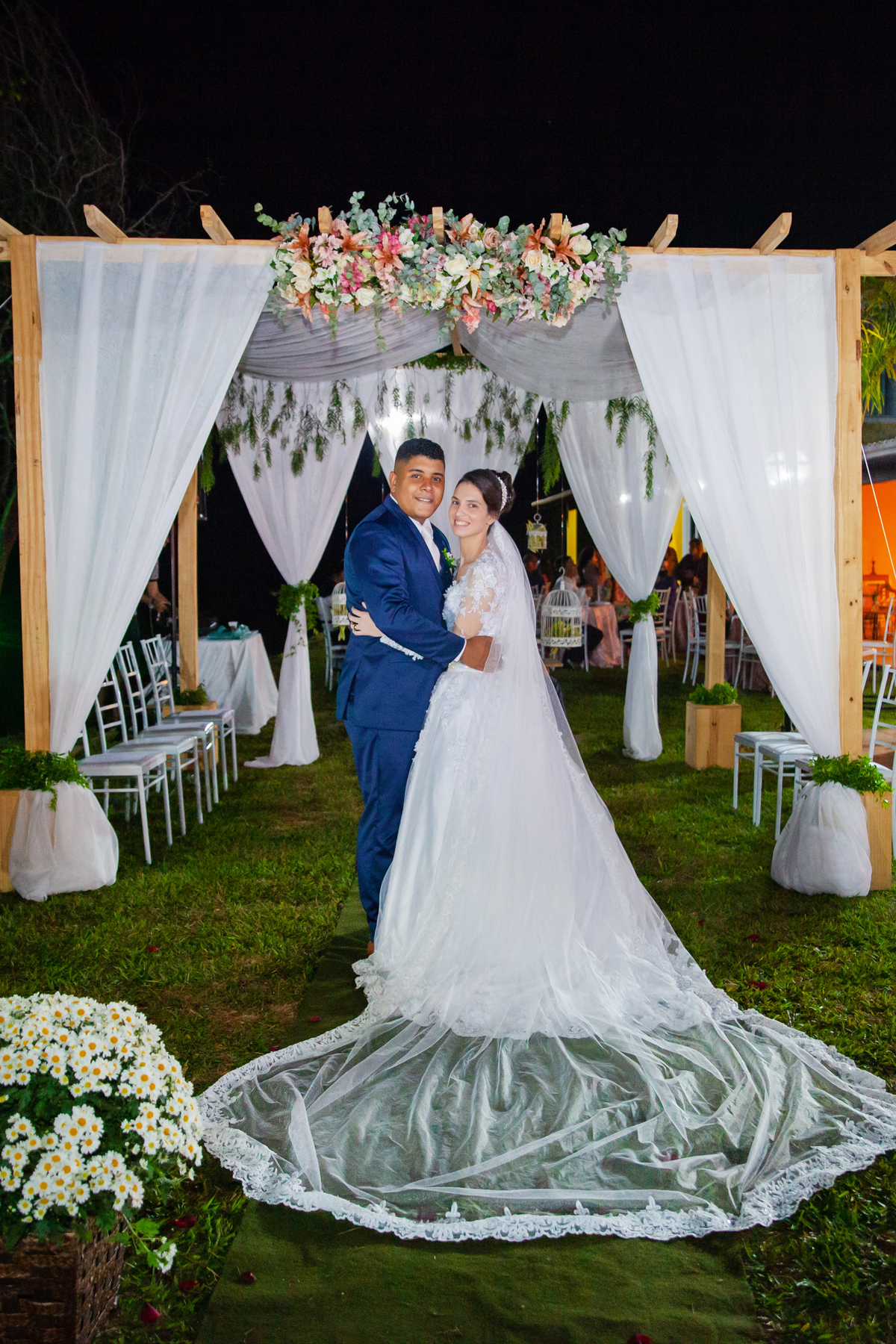 Noivos fazendo a sessão de fotos depois da cerimônia de casamento durante a festa em Santo Antônio de Pádua interior do Rio de Janeiro. Noiva com buquê em tons de rosa e noivo de terno azul escuro.