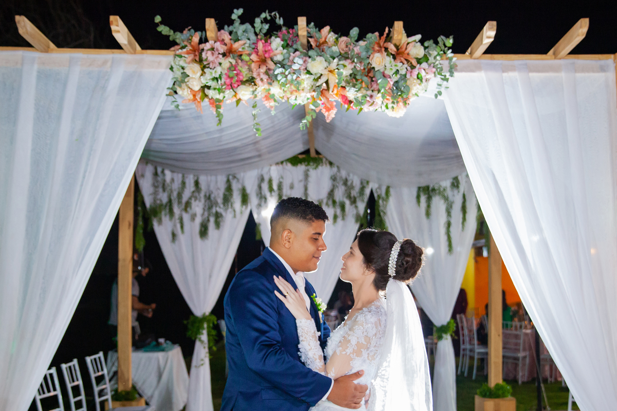 Noivos fazendo a sessão de fotos depois da cerimônia de casamento durante a festa em Santo Antônio de Pádua interior do Rio de Janeiro. Noiva com buquê em tons de rosa e noivo de terno azul escuro.