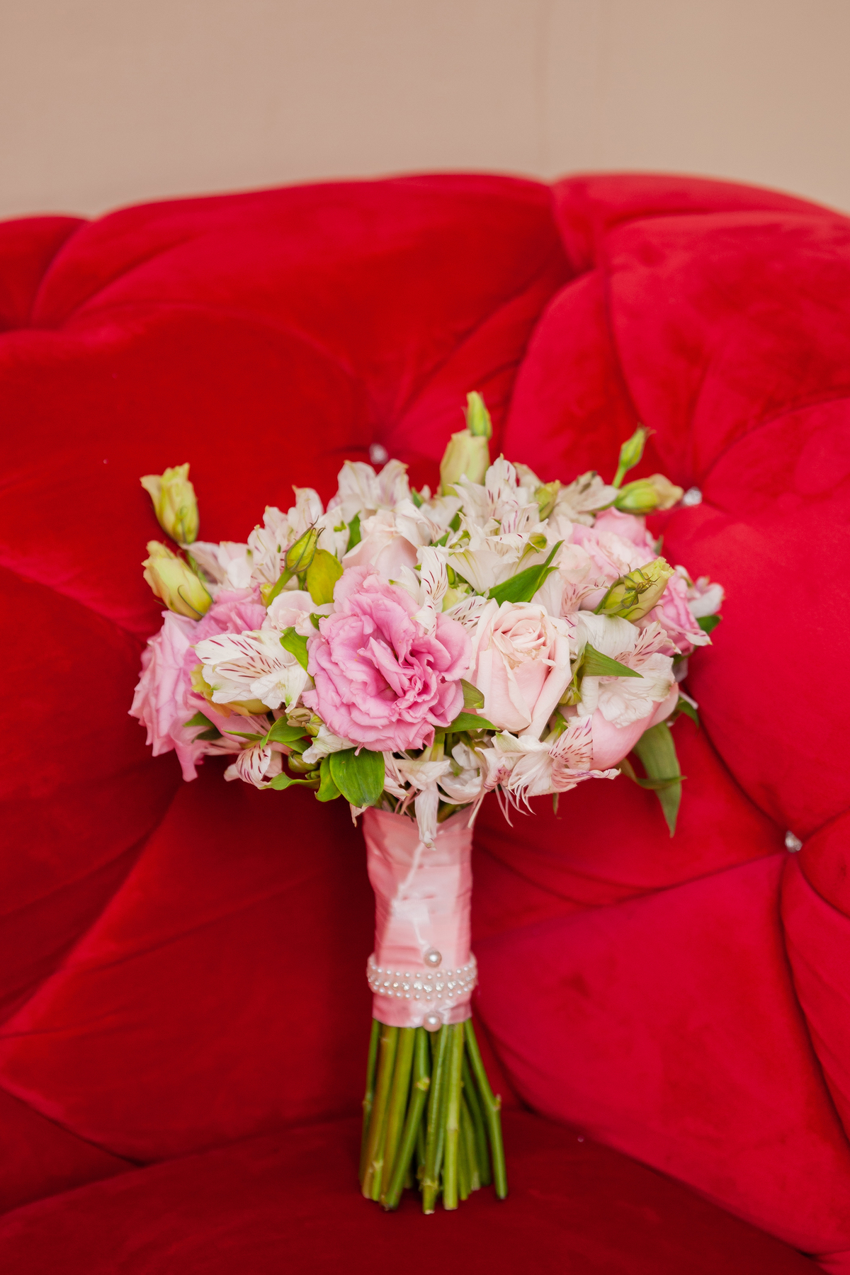 Buquê em tons de rosa em um sofá vermelho durante making of em salão de beleza em Pirapetinga para casamento em Santo Antônio de Pádua interior do Rio de Janeiro.