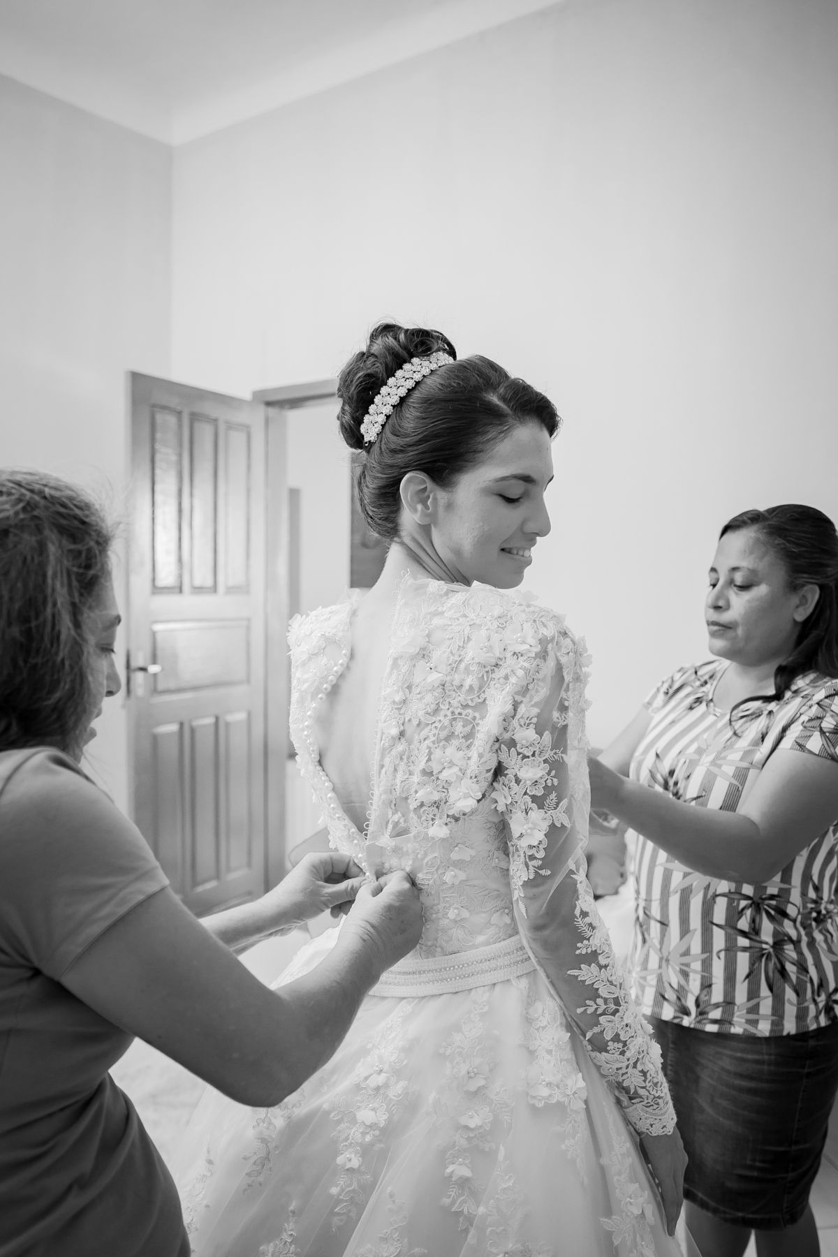 Foto em preto e branco da noiva se arrumando com sua mãe e sua sogra em salão de beleza momentos antes do casamento em salão de beleza em Pirapetinga para casamento em Santo Antônio de Pádua interior do Rio de Janeiro.