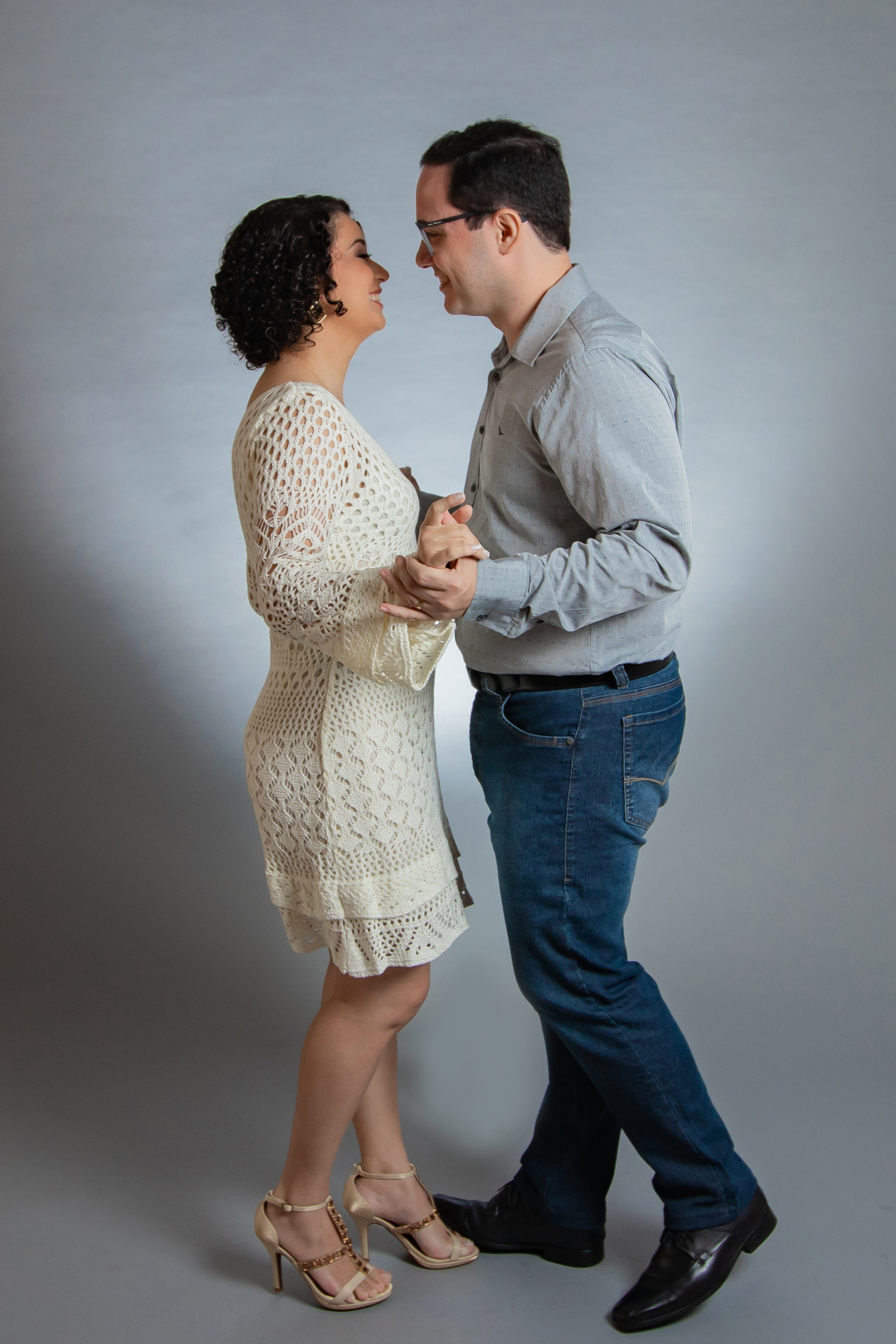Ensaio casal em estúdio fotográfico para comemorar 10 anos de casados. Foto do casal de mãos dadas sorrindo um para o outro. Ela com vestido branco de linha e ele de camisa social em stúdio em Santo Antônio de Pádua no interior do Rio de Janeiro.