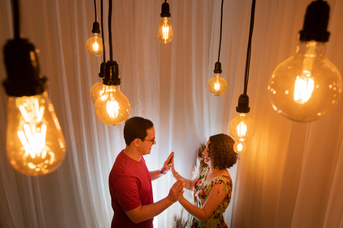 Ensaio casal em estúdio fotográfico para comemorar 10 anos de casados. Casal com roupas coloridas em cenário Em stúdio em Santo Antônio de Pádua no interior do Rio de Janeiro. Casal sorrindo muito feliz em cenário com lâmpadas penduradas.