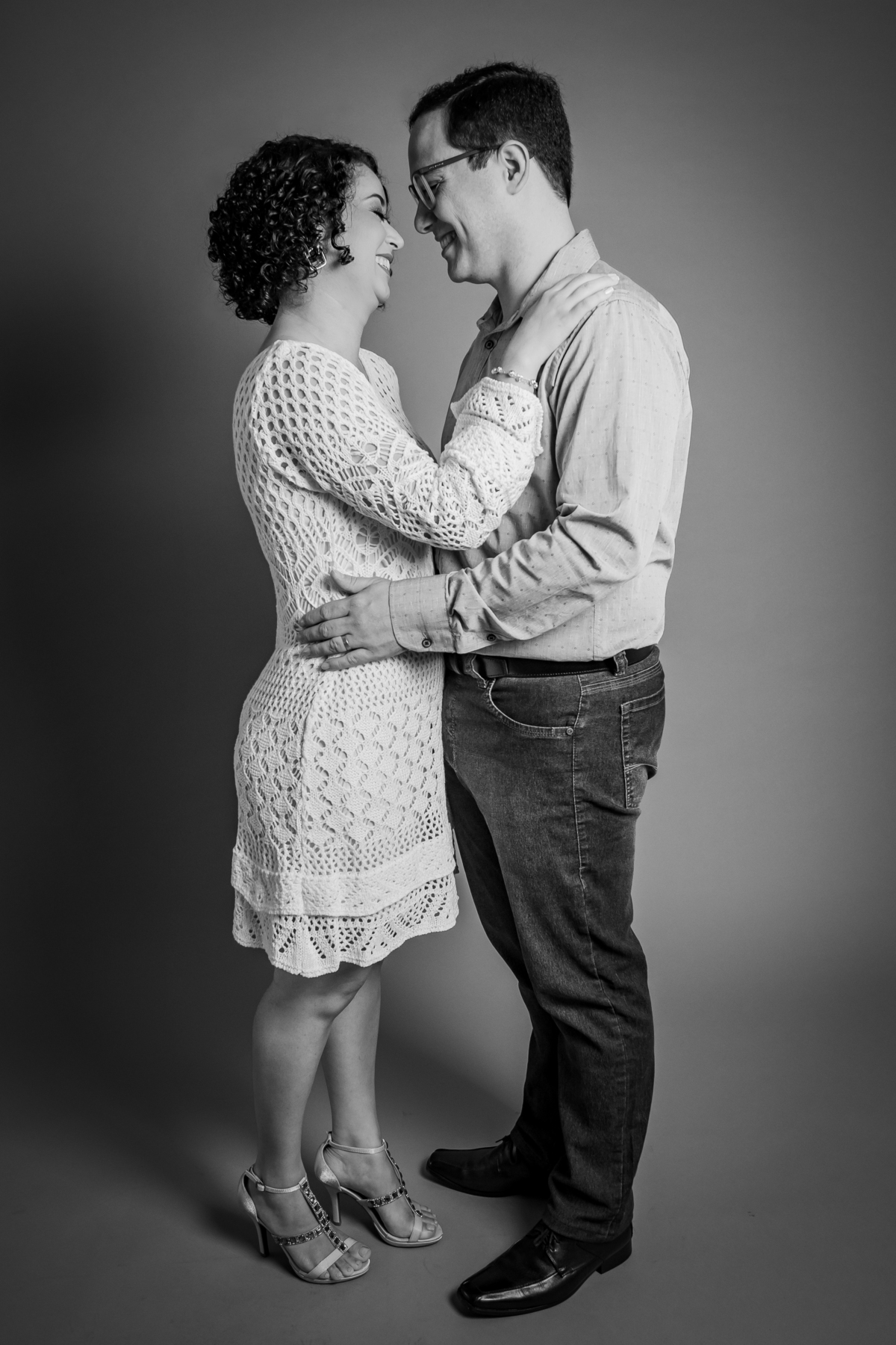 Ensaio casal em estúdio fotográfico para comemorar 10 anos de casados. Sorrindo um para o outro em foto preto e branco. Ela com vestido branco de linha e ele de camisa social em stúdio em Santo Antônio de Pádua no interior do Rio de Janeiro.