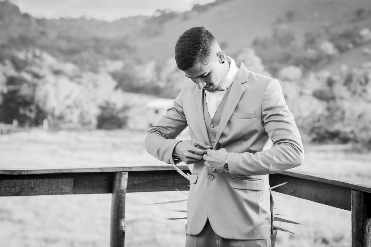 Making of do noivo ao ar livre, com terno dourado e gravata de borboleta em casamento durante o dia em Santo Antônio de Pádua no interior do Rio de Janeiro. Foto em preto e branco.