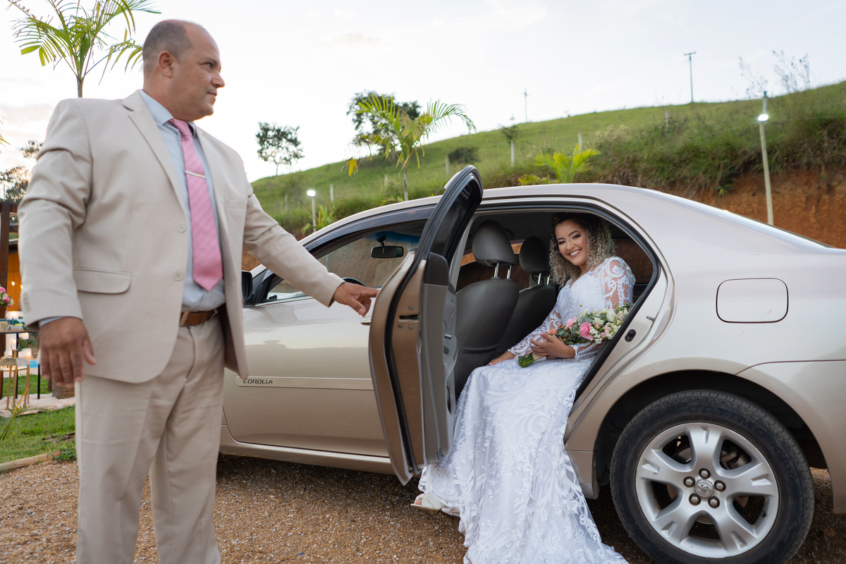 Noiva linda de mãos dadas com seu pai saindo do carro para a cerimônia de casamento durante o dia em Santo Antônio de Pádua no interior do Rio de Janeiro.