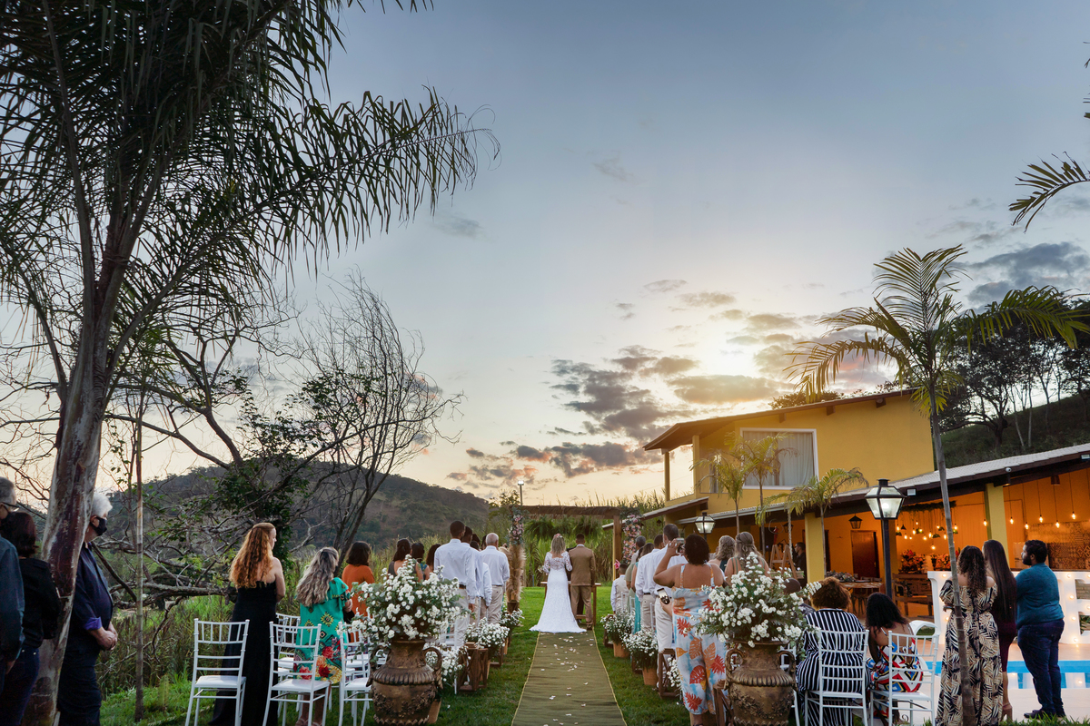 Noivos felizes durante cerimonia de casamento ao ar livre, noiva com vestido sereia e noivo com terno dourado e gravata borboleta. Casamento durante o dia com um pôr do sol maravilhoso em Santo Antônio de Pádua no interior do Rio de Janeiro.