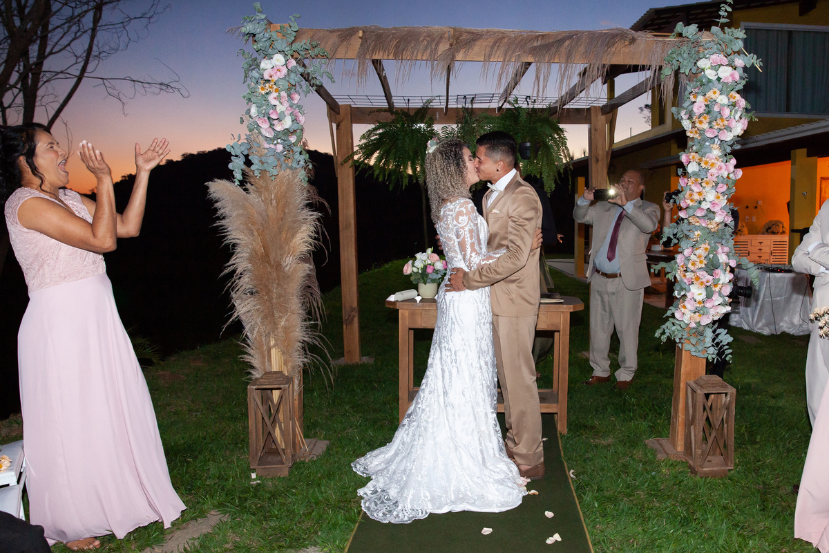 Noivos felizes se beijando durante cerimonia de casamento ao ar livre, noiva com vestido sereia e noivo com terno dourado e gravata borboleta. Casamento durante o dia com um pôr do sol maravilhoso em Santo Antônio de Pádua no interior do Rio de Janeiro.