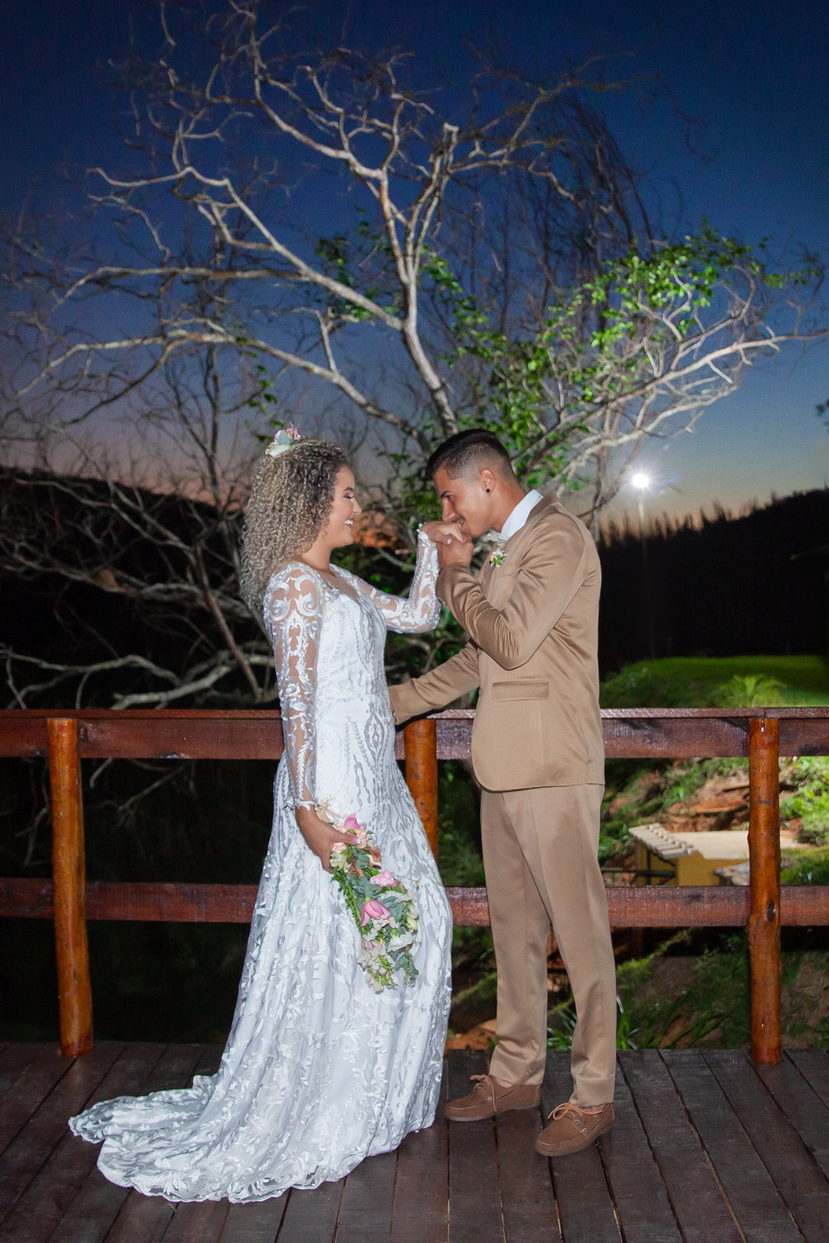 Noivo beijando a mão da noiva durante sessão de fotos ao pôr do sol maravilhoso em um píer em casamento durante o dia ao ar livre  em Santo Antônio de Pádua no interior do Rio de Janeiro.