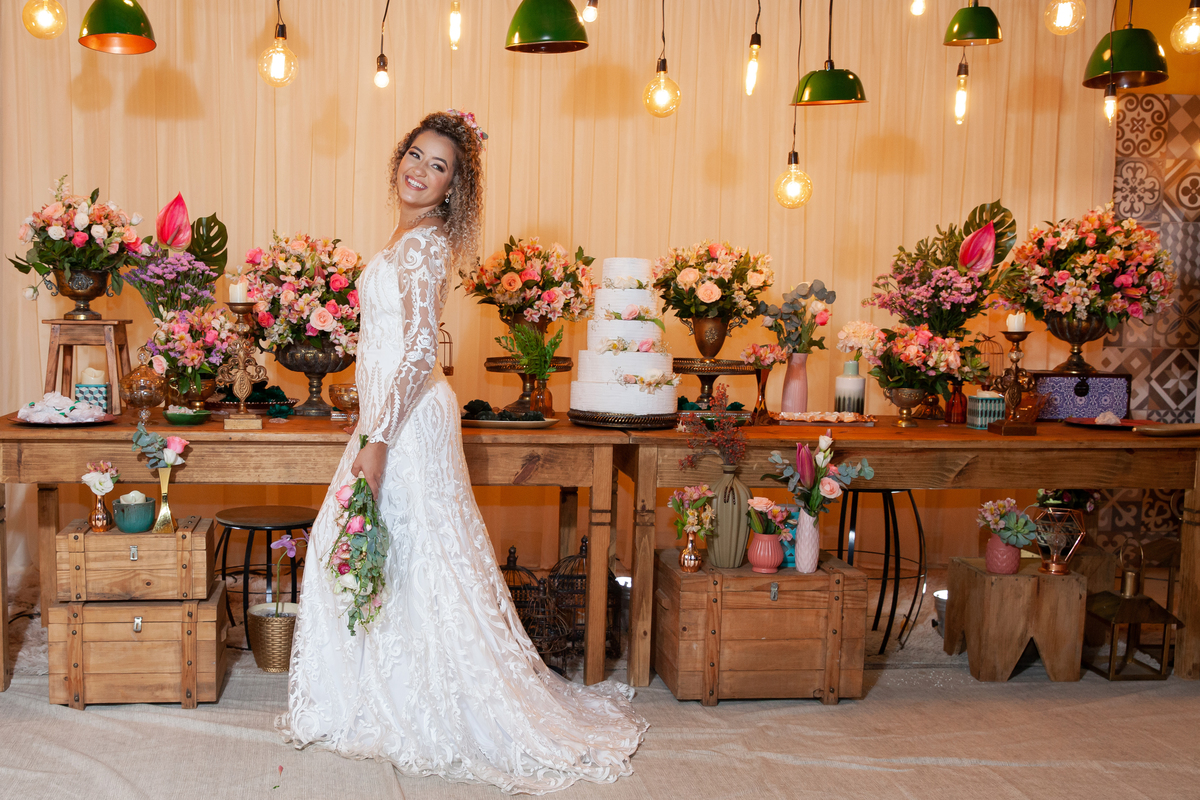 Noiva com vestido sereia, muito feliz  no meio da decoração de casamento, com lâmpadas penduradas, moveis rústicos e flores coloridas. Casamento durante o dia ao ar livre  em Santo Antônio de Pádua no interior do Rio de Janeiro.
