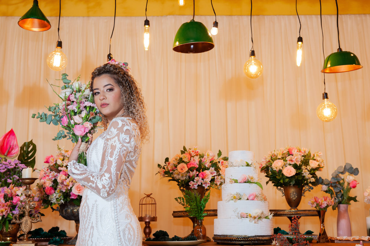 Noiva com vestido sereia, muito feliz  no meio da decoração de casamento, com lâmpadas penduradas, moveis rústicos e flores coloridas. Casamento durante o dia ao ar livre  em Santo Antônio de Pádua no interior do Rio de Janeiro.