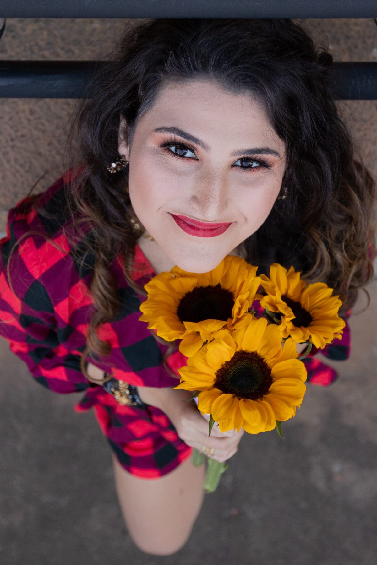Ensaio de 15 , debutante sorrindo,  vestindo roupa xadrez e segurando flores girassóis em um dia ensolarado em Santo Antônio de Pádua no interior do Rio de Janeiro.