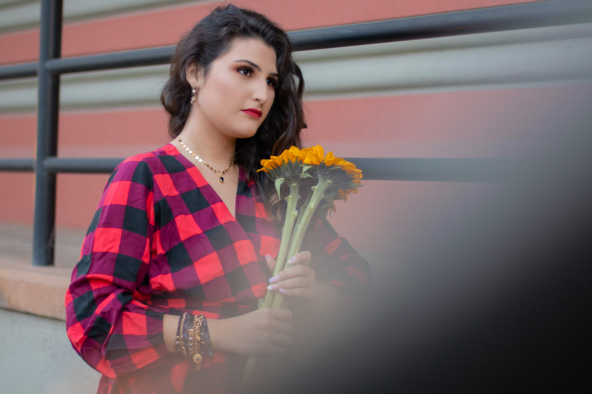 Ensaio de 15 , debutante sorrindo,  vestindo roupa xadrez e segurando flores girassóis em um dia ensolarado em Santo Antônio de Pádua no interior do Rio de Janeiro.