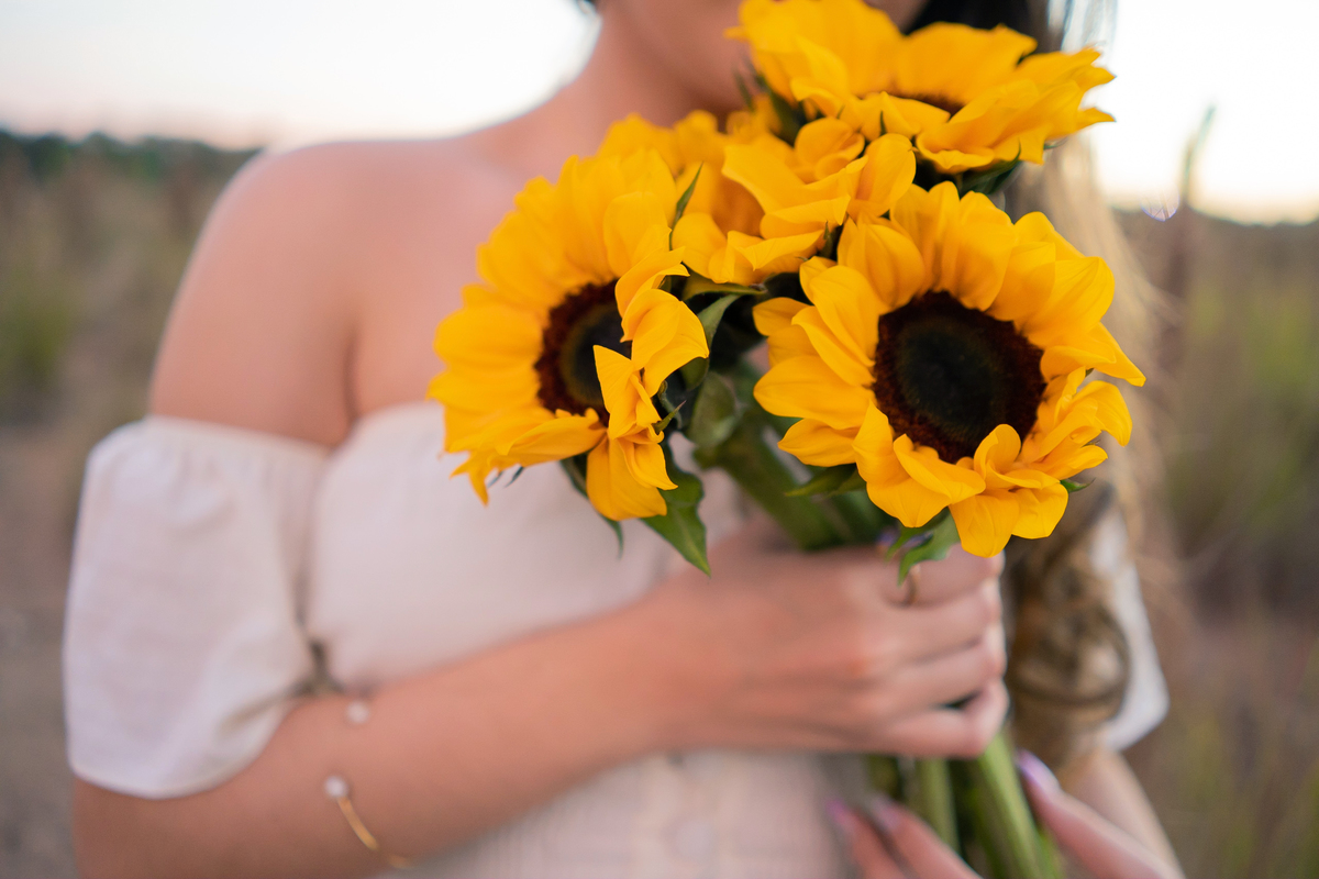 Ensaio de 15 , debutante sorrindo,  com vestido branco em um lindo pôr do sol segurando flores de girassol em Pádua interior do Rio de Janeiro.