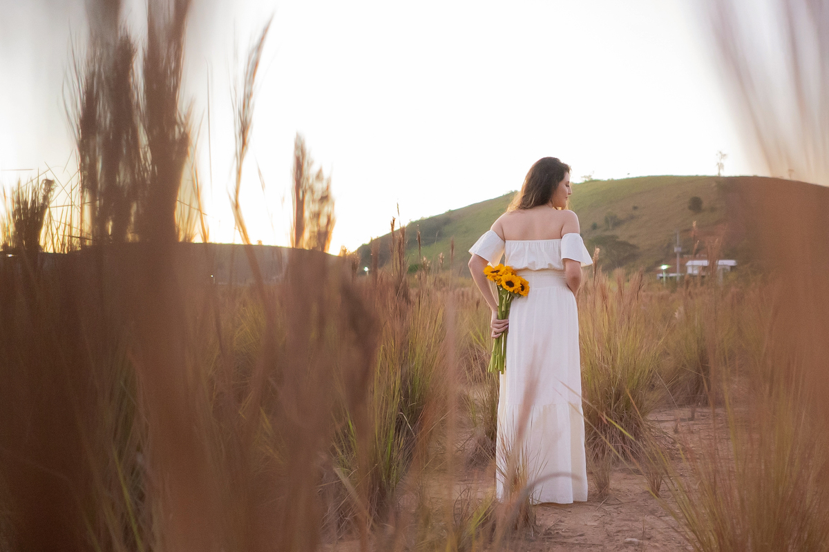 Ensaio de 15 , debutante sorrindo,  com vestido branco em um lindo pôr do sol segurando flores de girassol em Pádua interior do Rio de Janeiro.