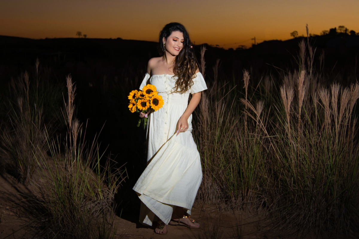 Ensaio de 15 , debutante sorrindo,  com vestido branco em um lindo pôr do sol segurando flores de girassol em Pádua interior do Rio de Janeiro.
