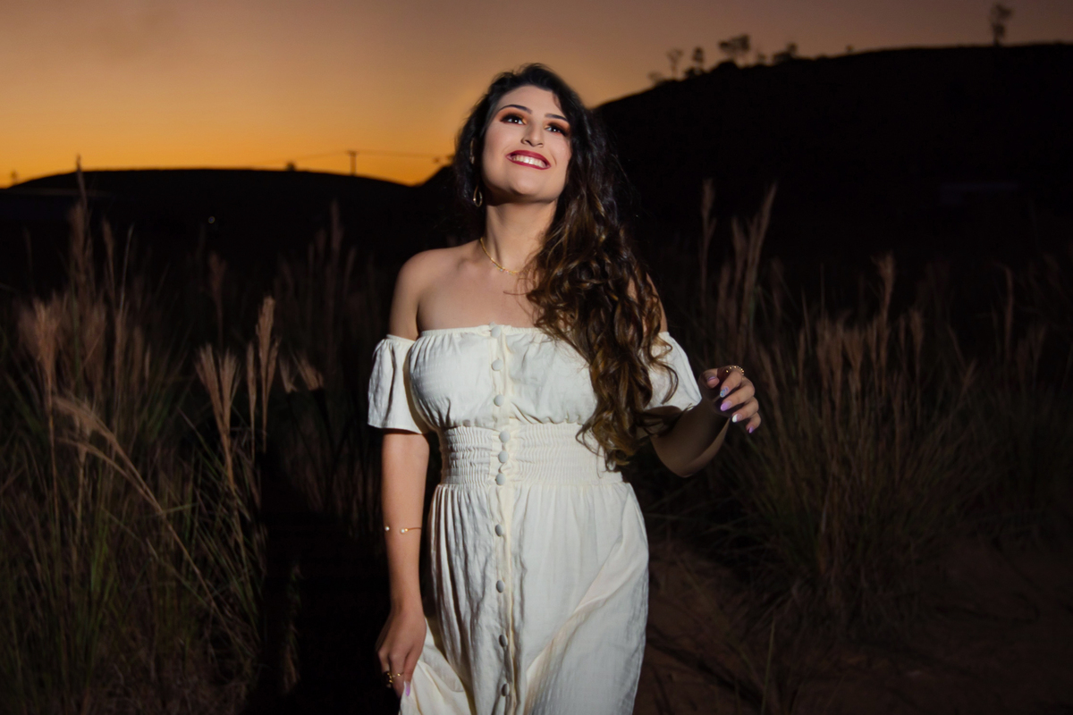 Ensaio de 15 , debutante sorrindo,  com vestido branco em um lindo pôr do sol segurando flores de girassol em Pádua interior do Rio de Janeiro.