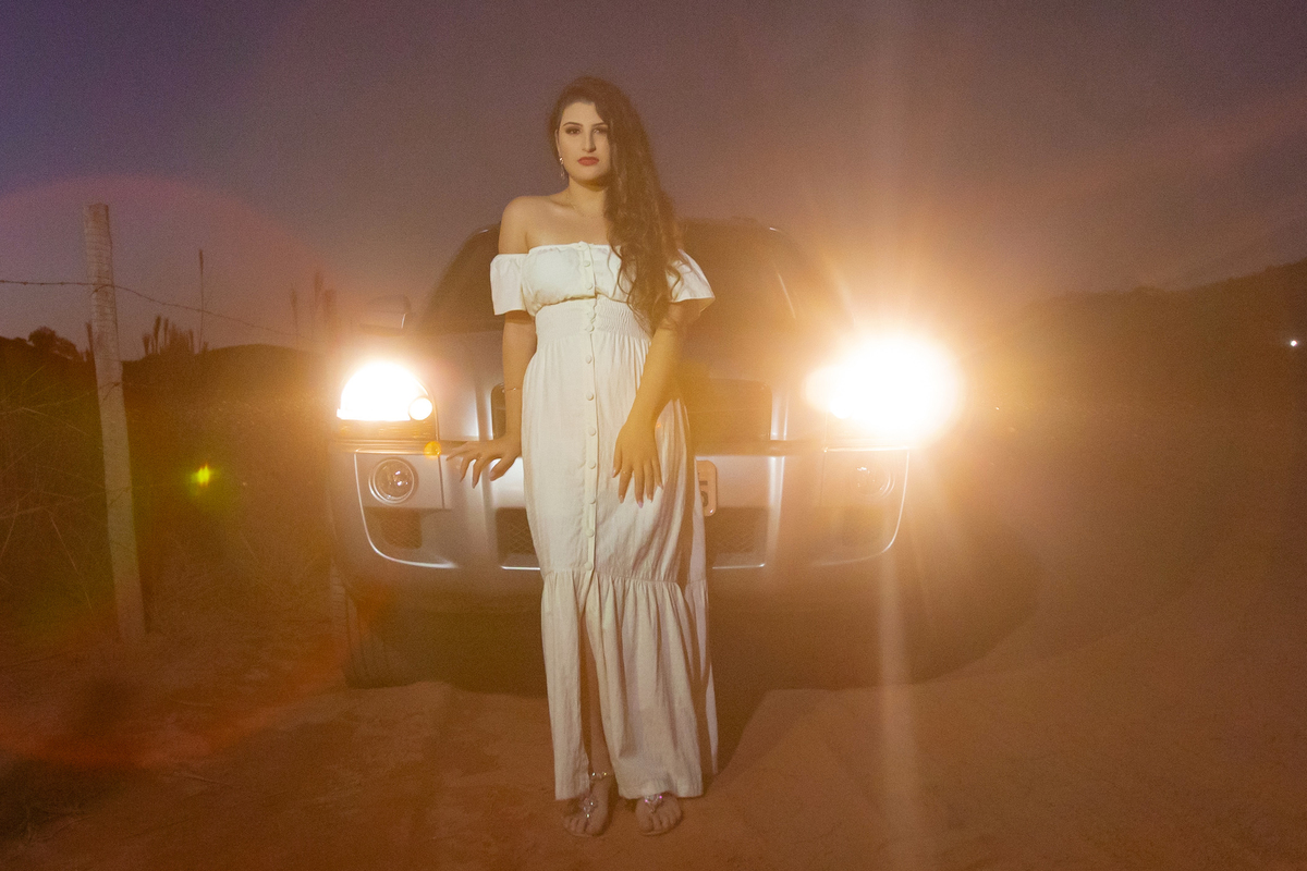 Ensaio de 15 , debutante sorrindo,  com vestido branco em um lindo pôr do sol na frente de um carro em Pádua interior do Rio de Janeiro.