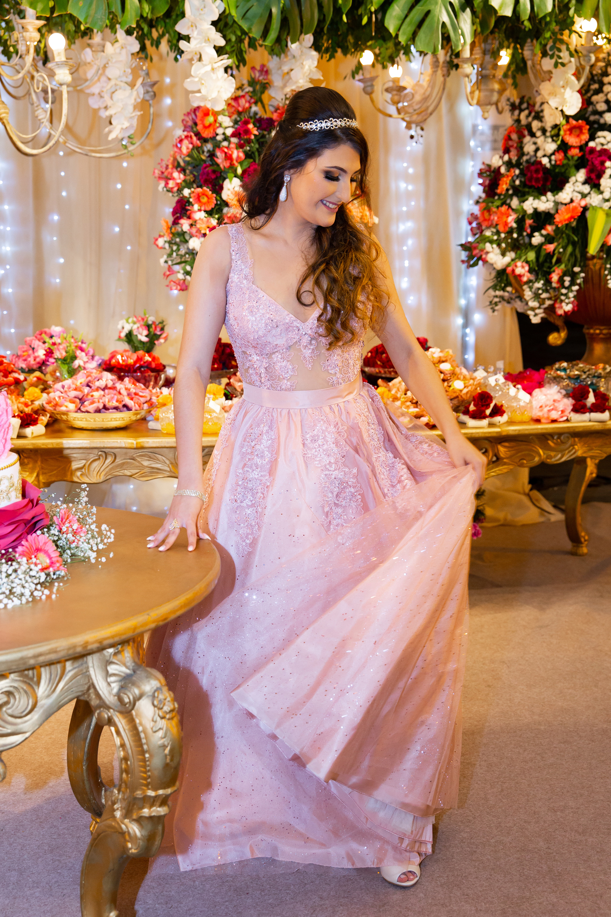 Debutante linda e feliz posando para foto na mesa do bolo de 5 andares em tons de rosa, vermelho, brando e dourado em salão de festa maison saintec ecile em Santo Antônio de Pádua interior do Rio de Janeiro.