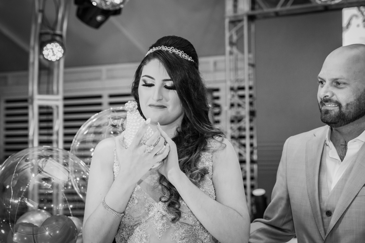 Foto em preta e branca de debutante emocionada segurando imagem de nossa Senhora durante a festa em salão de festa maison sainte cecile em Santo Antônio de Pádua interior do Rio de Janeiro.