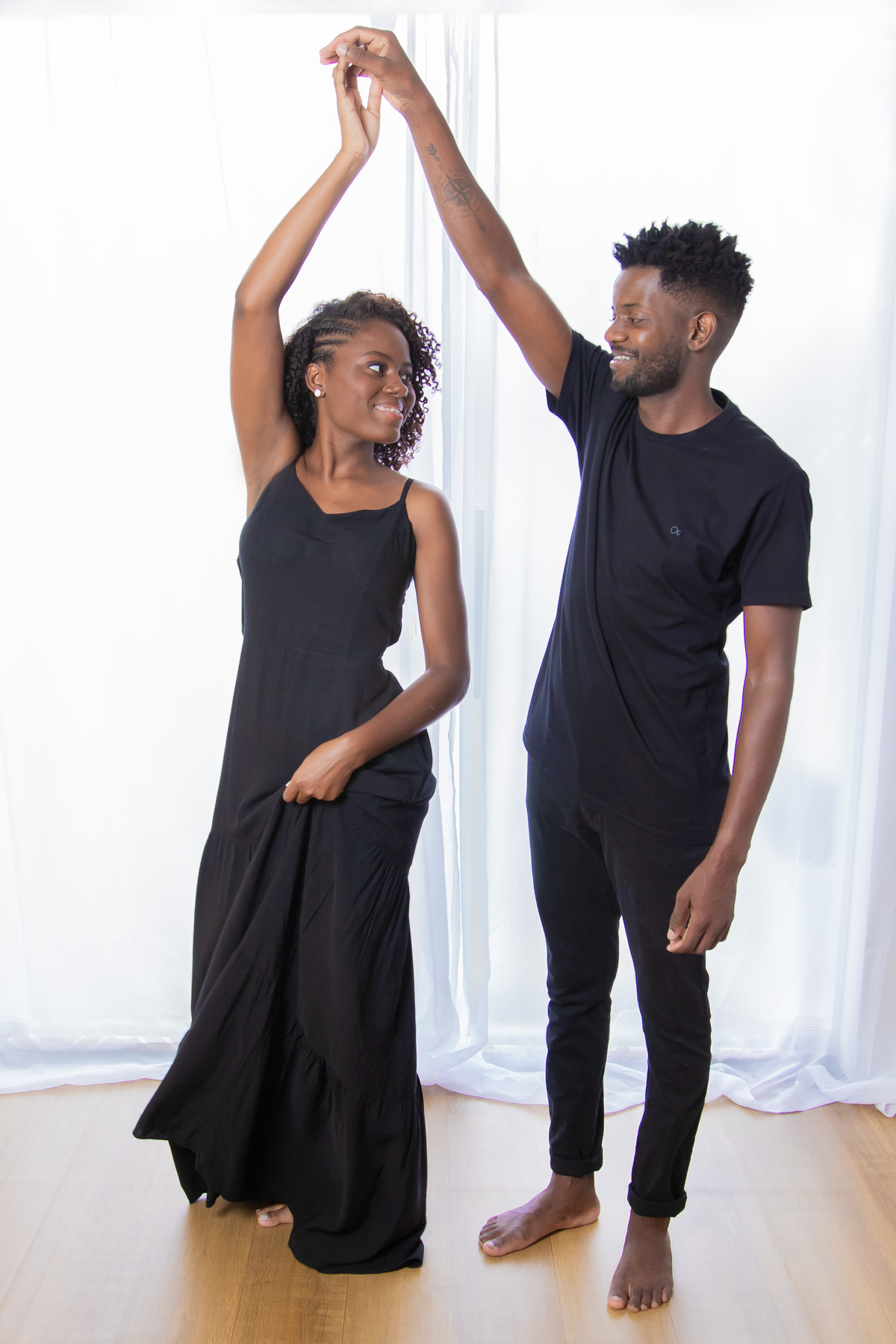 Noiva e noivo com roupas pretas em ensaio pré casamento em estúdio em Santo Antônio de Pádua – RJ. Noiva com buquê de rosas brancas e muito feliz em cenário de flores secas e desidratadas.  Noiva dançando com o noivo. 