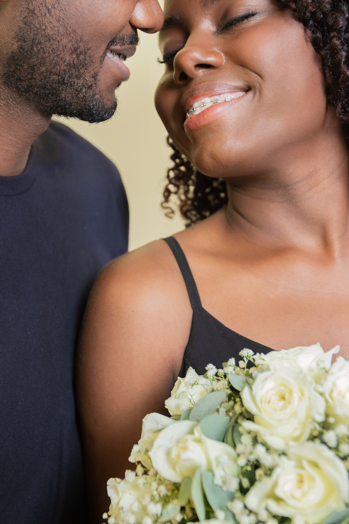 Noiva e noivo com roupas pretas em ensaio pré casamento em estúdio em Santo Antônio de Pádua – RJ. Noiva com buquê de rosas brancas e muito feliz e com o rostinho bem coladinhos. 