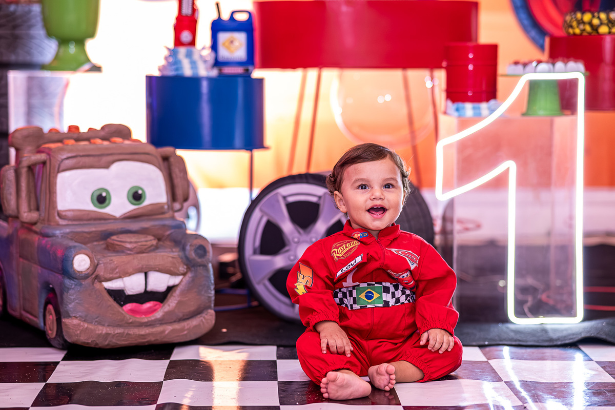 evi, o aniversariante de 1 ano, brincando com um carrinho de brinquedo no chão da festa.