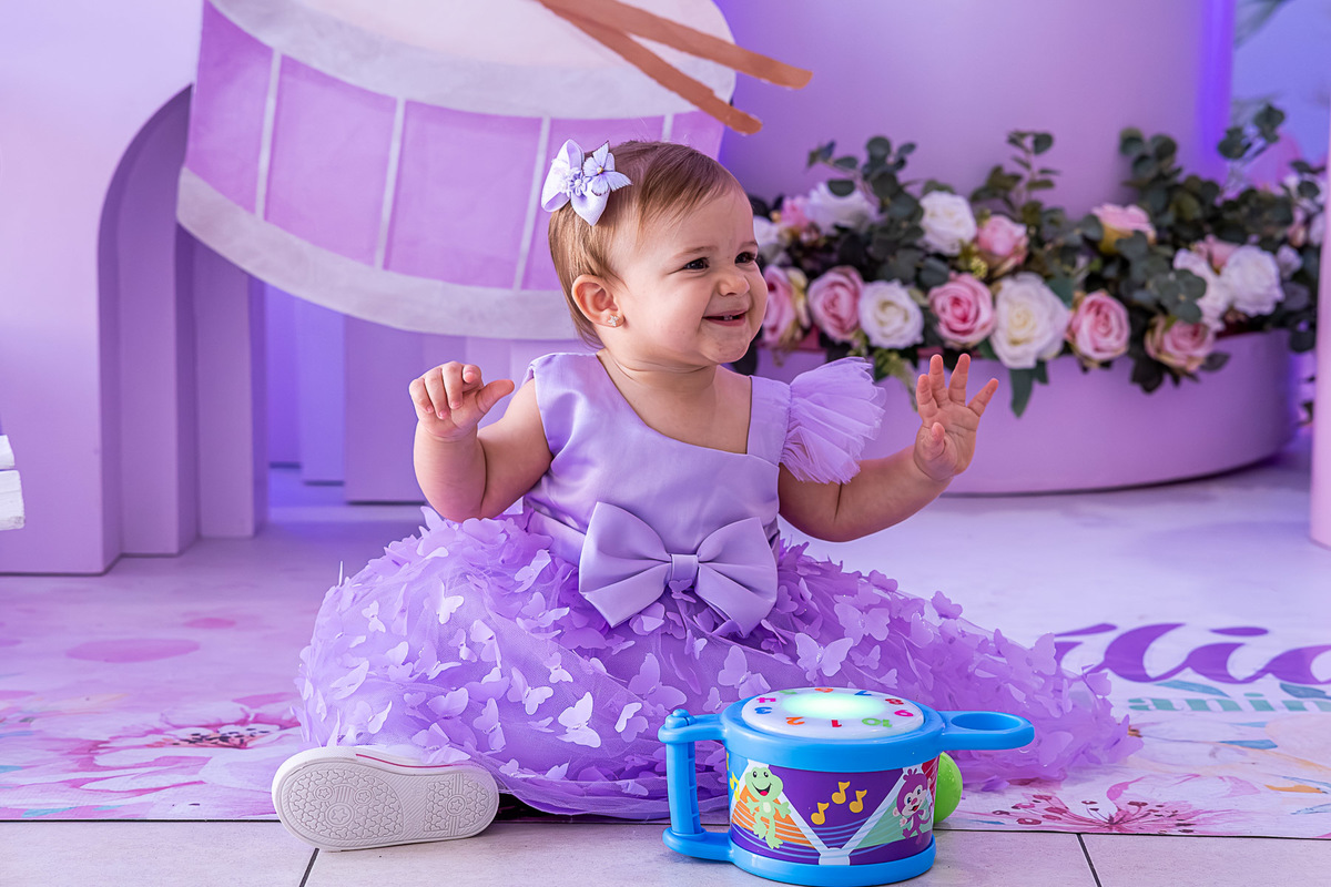  Cecília sentada, explorando a decoração do seu 1º aniversário, tema Turnê Encantada.