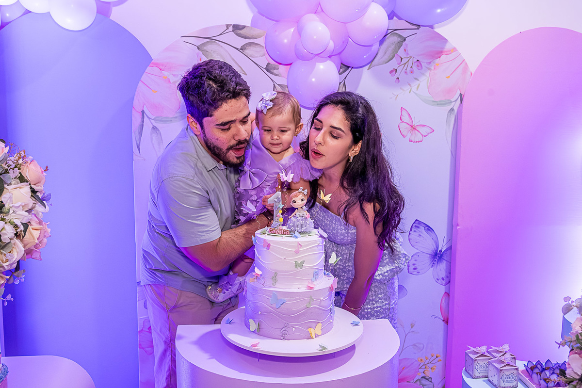 Cecília no colo dos pais, com o bolo de aniversário ao fundo, durante o parabéns.