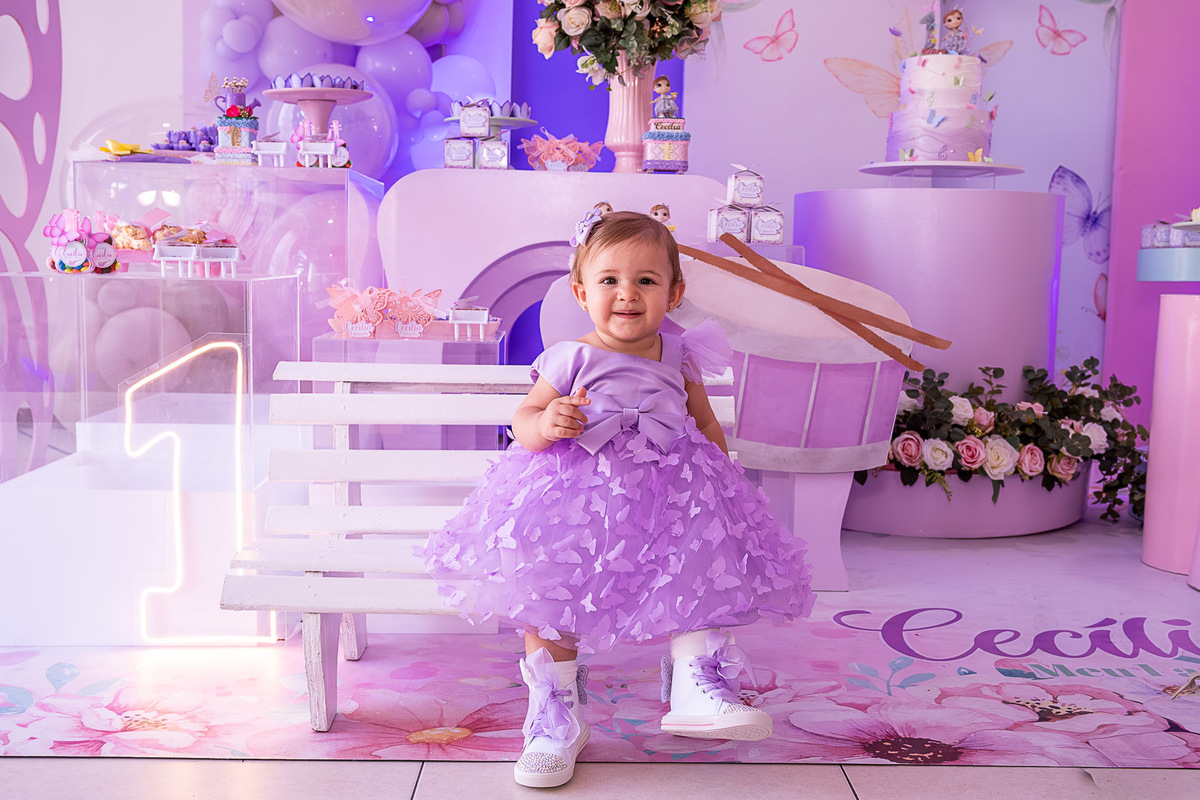 Cecília sentada, em um momento espontâneo de alegria, com a decoração do Jardim das Borboletas.