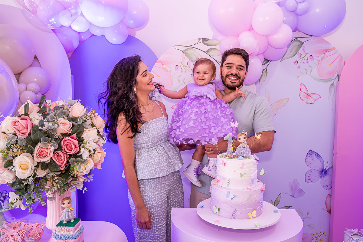 Cecília no colo dos pais, olhando para a decoração do Jardim das Borboletas.