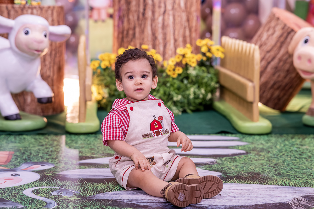 Renan, o aniversariante de 1 ano, sorrindo na frente da decoração Fazendinha, no Castelo Encantado, Vilas do Atlântico.