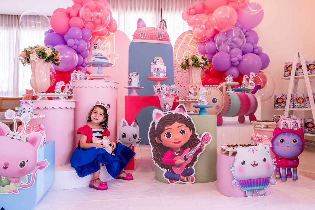 Heloísa sozinha, com um olhar curioso para a câmera, em frente à decoração da 