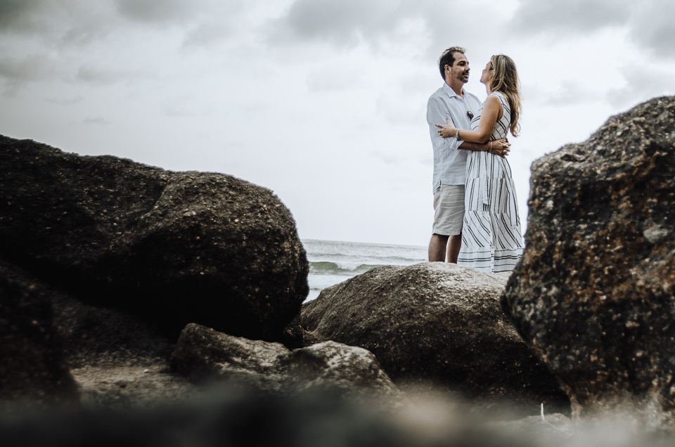 foto do casal posando entre as pedras na encosta da praia