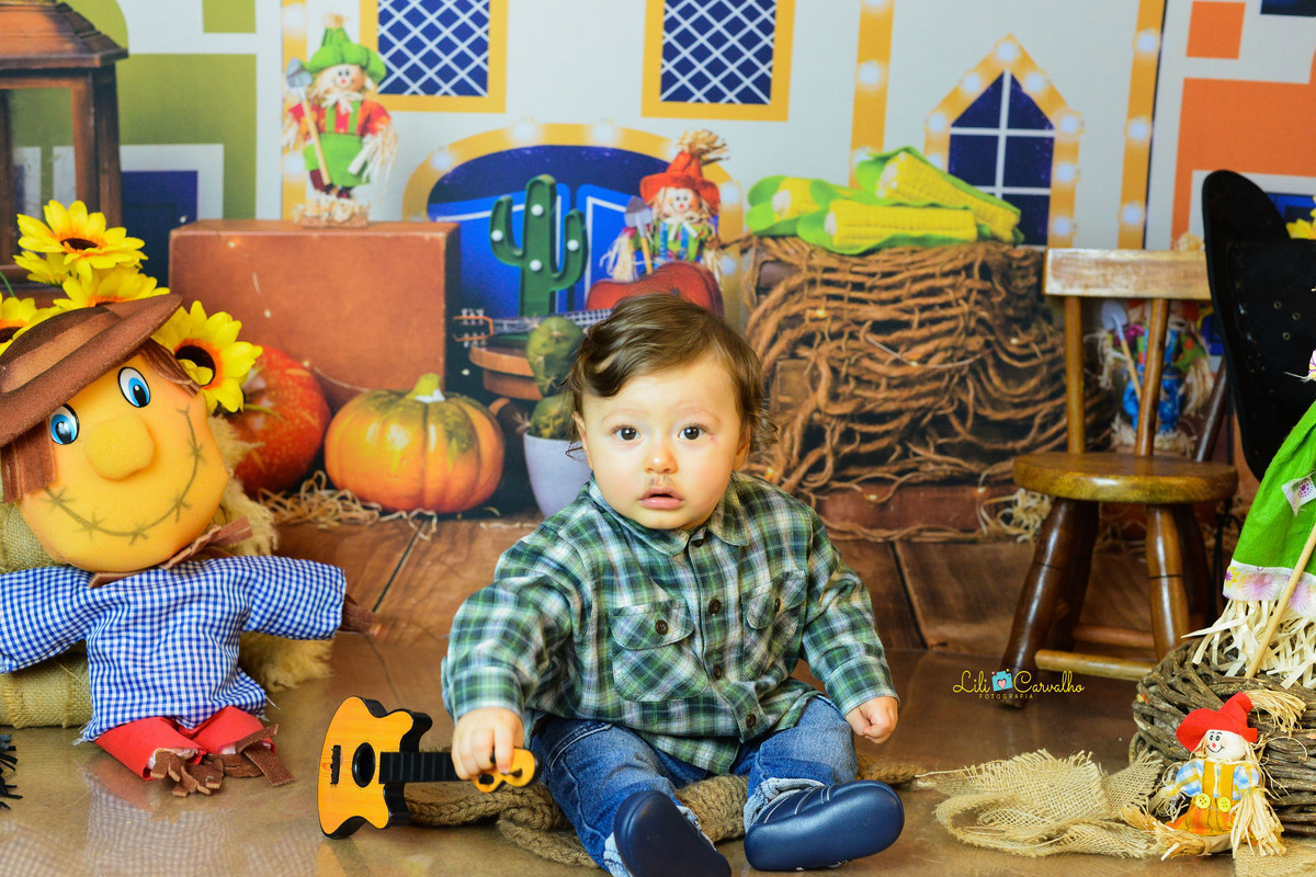 ensaio fotográfico realizado em estudio de menino, tema junino, camisa xadrez, violao