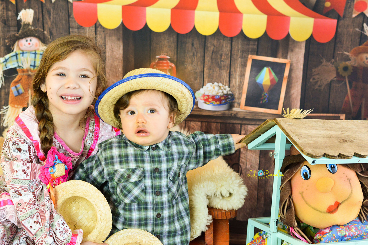 ensaio fotográfico realizado em estudio de menino, tema junino, camisa xadrez com irma de rosa