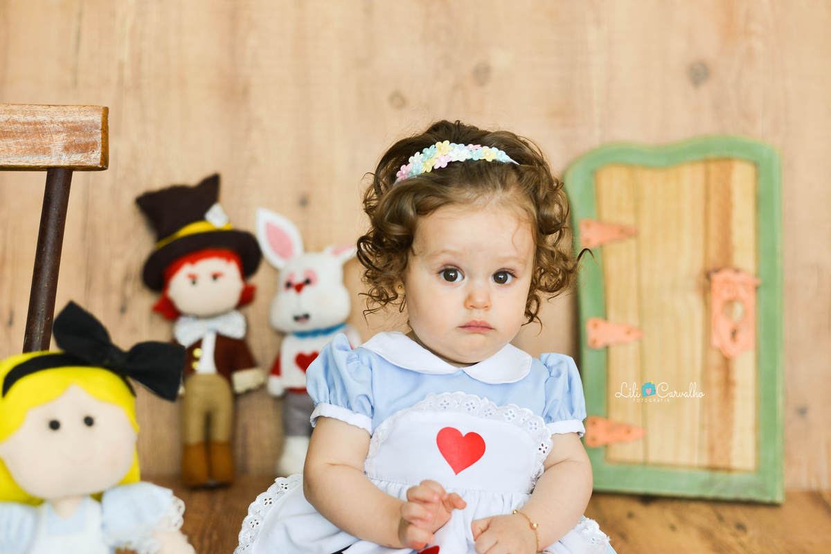 criança sentada, vestida de Alice no país das maravilhas, com cara de surpresa