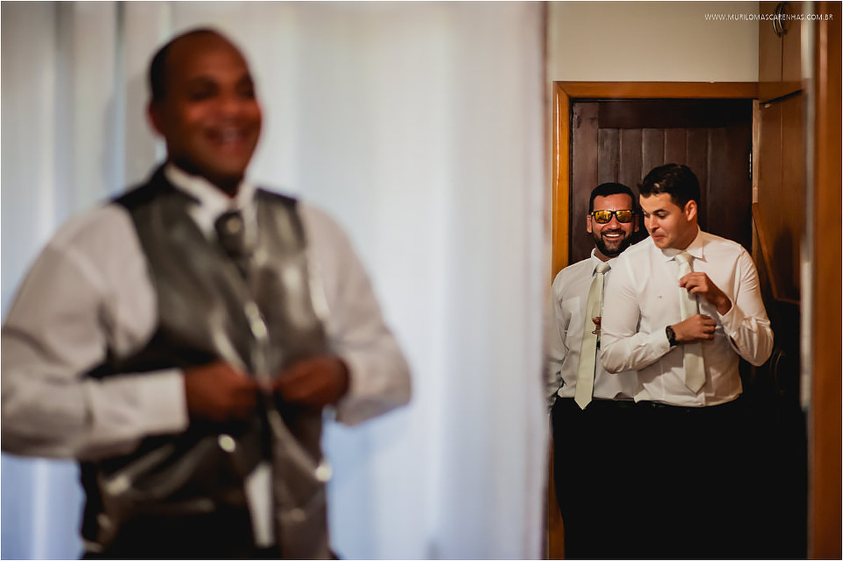 Noivo observando padrinhos brincarem, enquanto coloca o colete