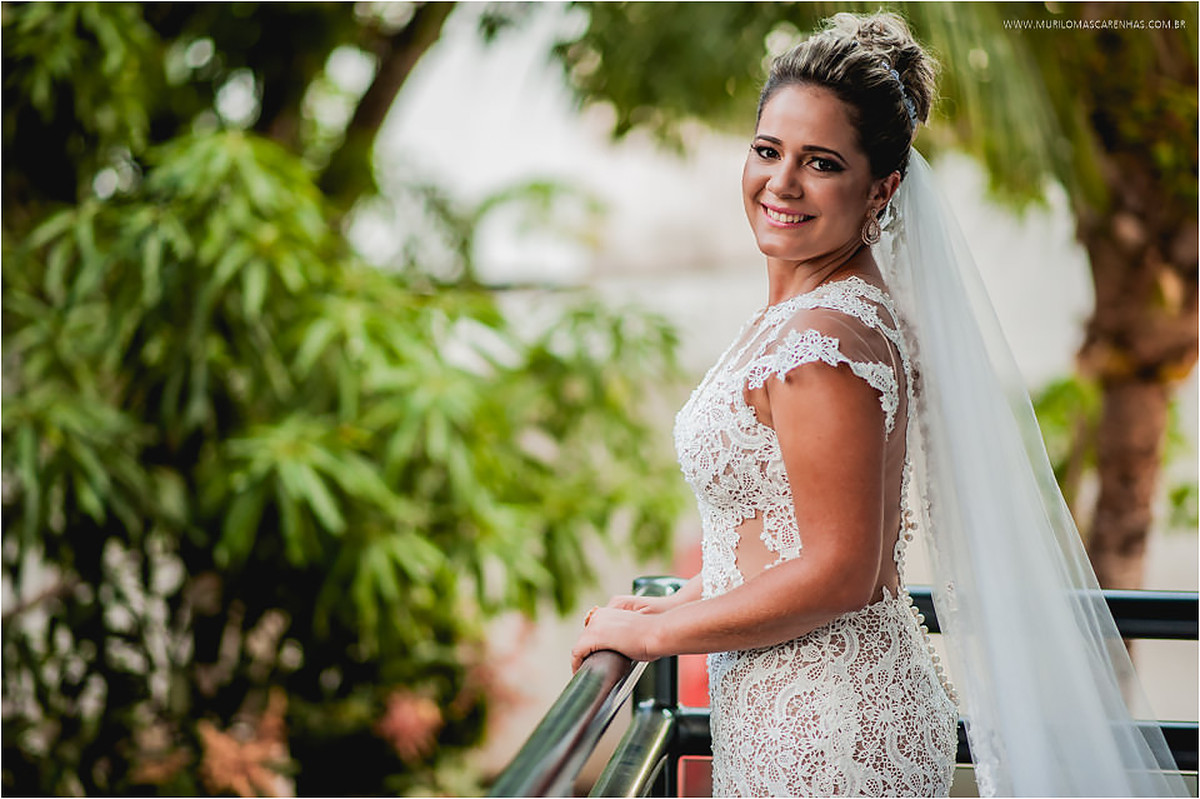 Noiva pronta para casamento de dia, na sacada do quarto, com vestido de renda e véu comprido
