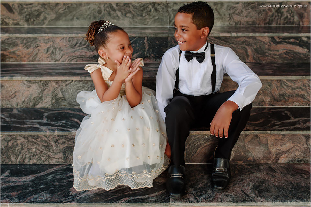 Daminha e pajem conversam e sorriem sentados na escadaria