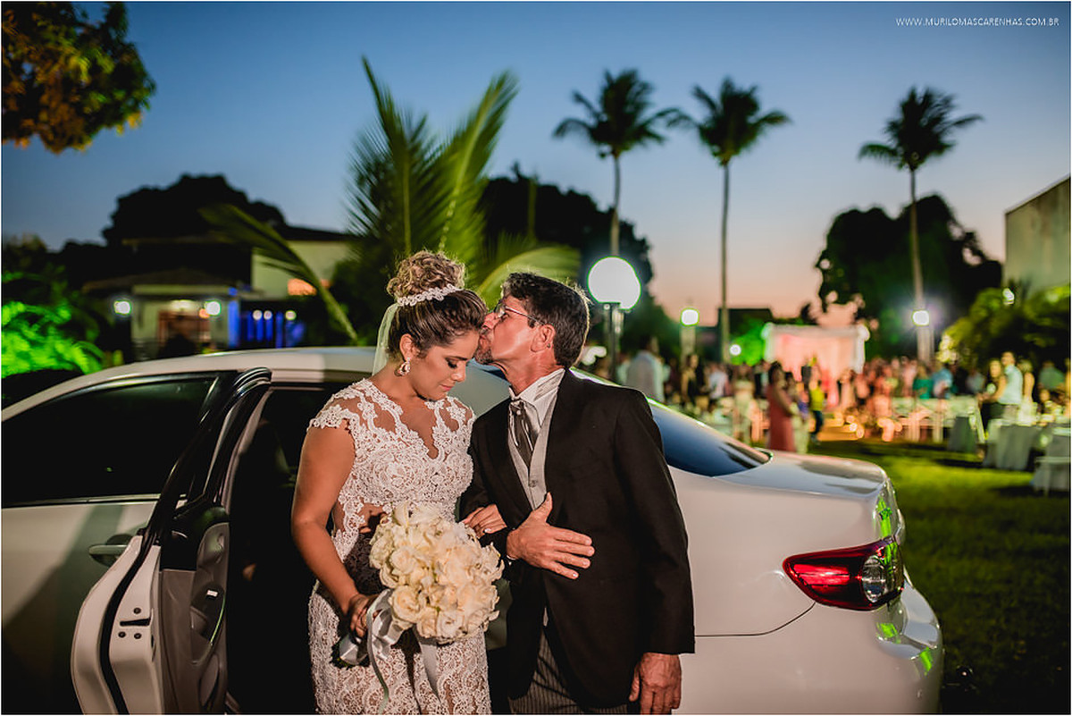 Pai da noiva beija a testa da filha em frente ao carro, na entrada da cerimônia