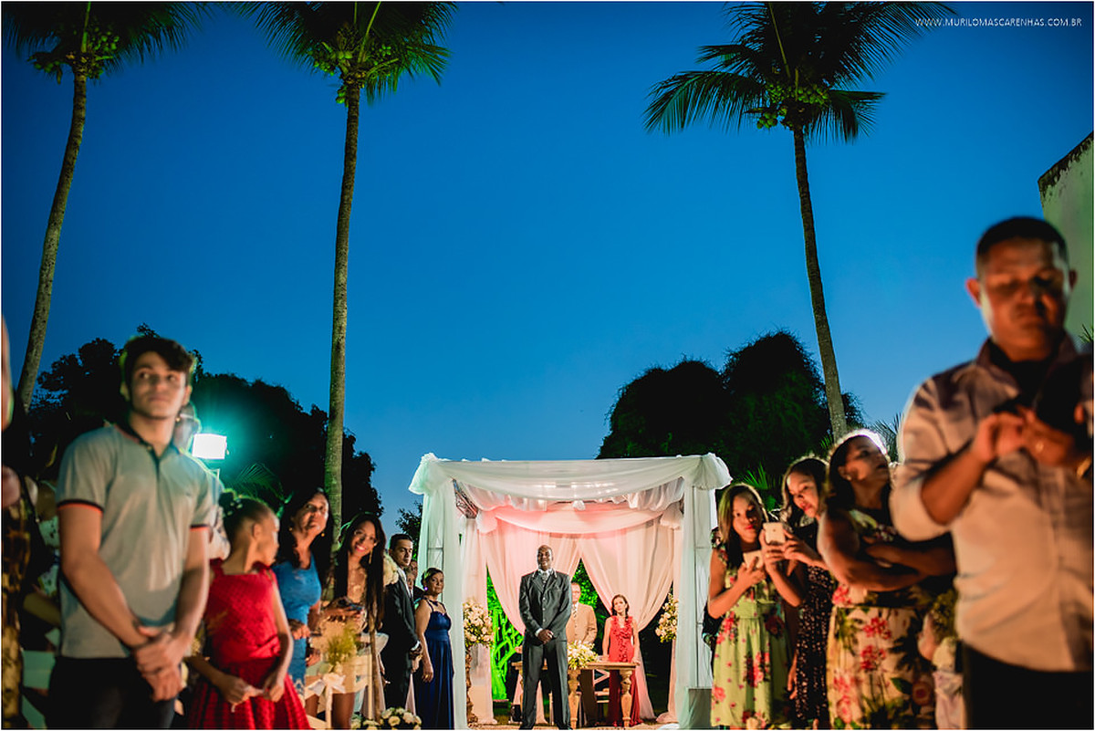 Noivo e convidados observam a entrada da noiva, embaixo da tenda do altar, durante o por do sol