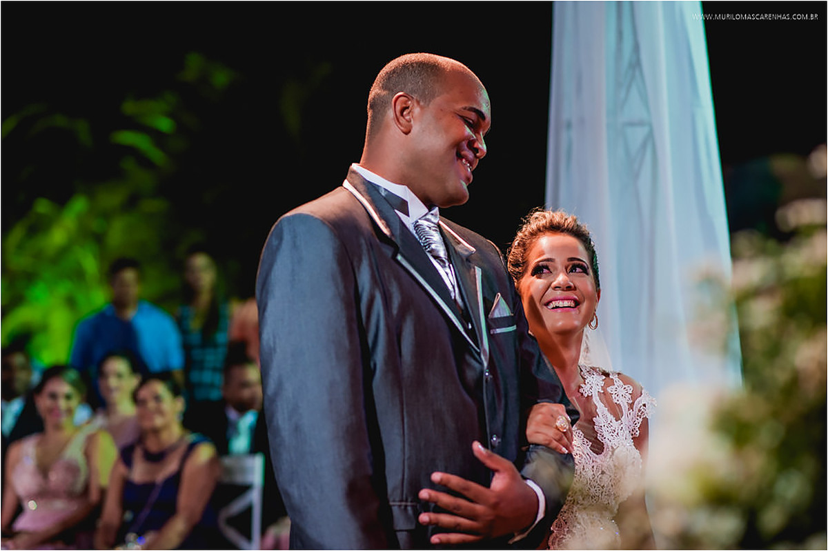 Noivo e noiva se olham e sorriem no altar