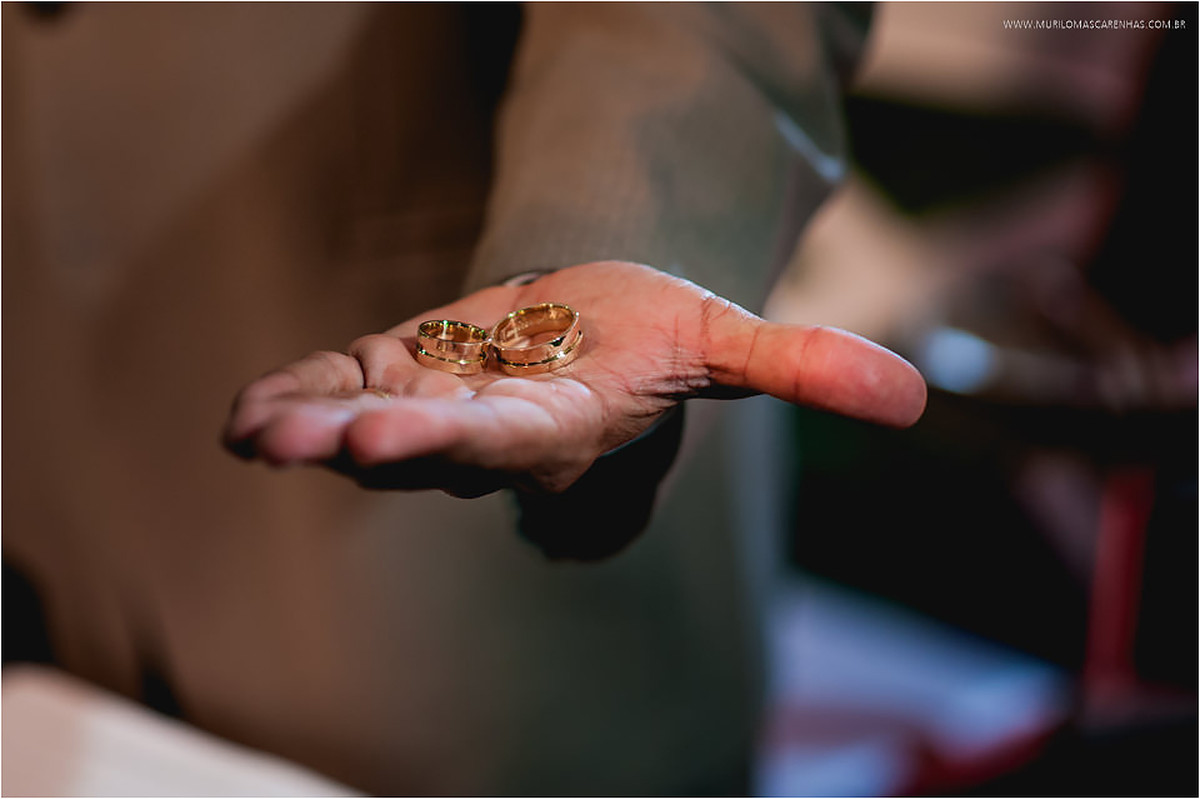 Mão do celebrante segura as alianças durante a benção