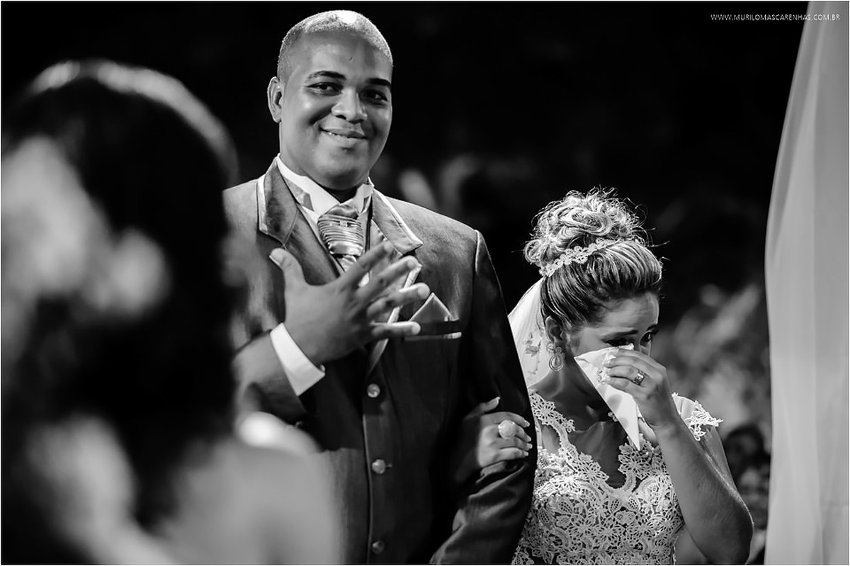 Noivo mostra a mão aberta, indicando o número cinco enquanto a noiva enxuga as lágrimas