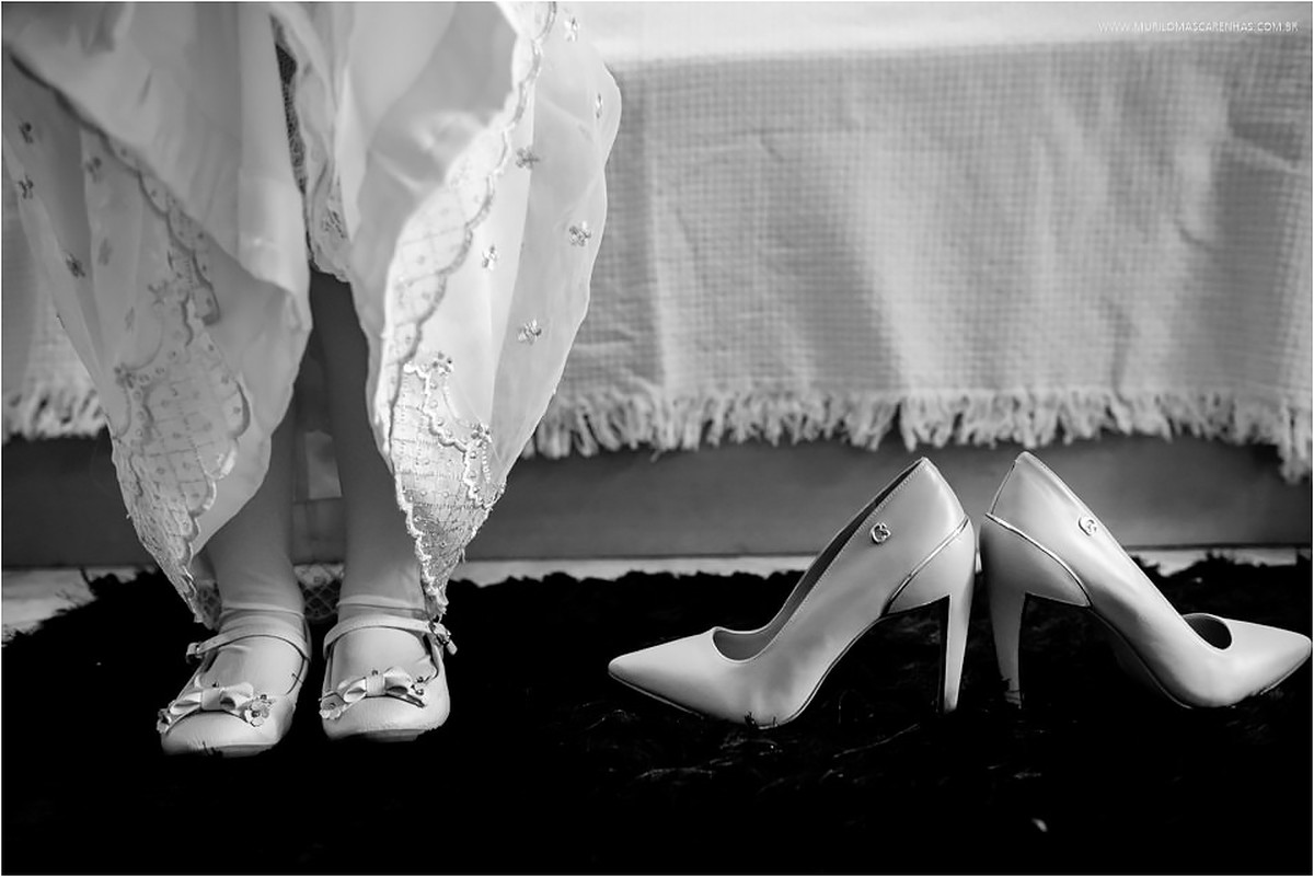 Pés da daminha com vestido levantado ao lado do sapato escarpin da noiva