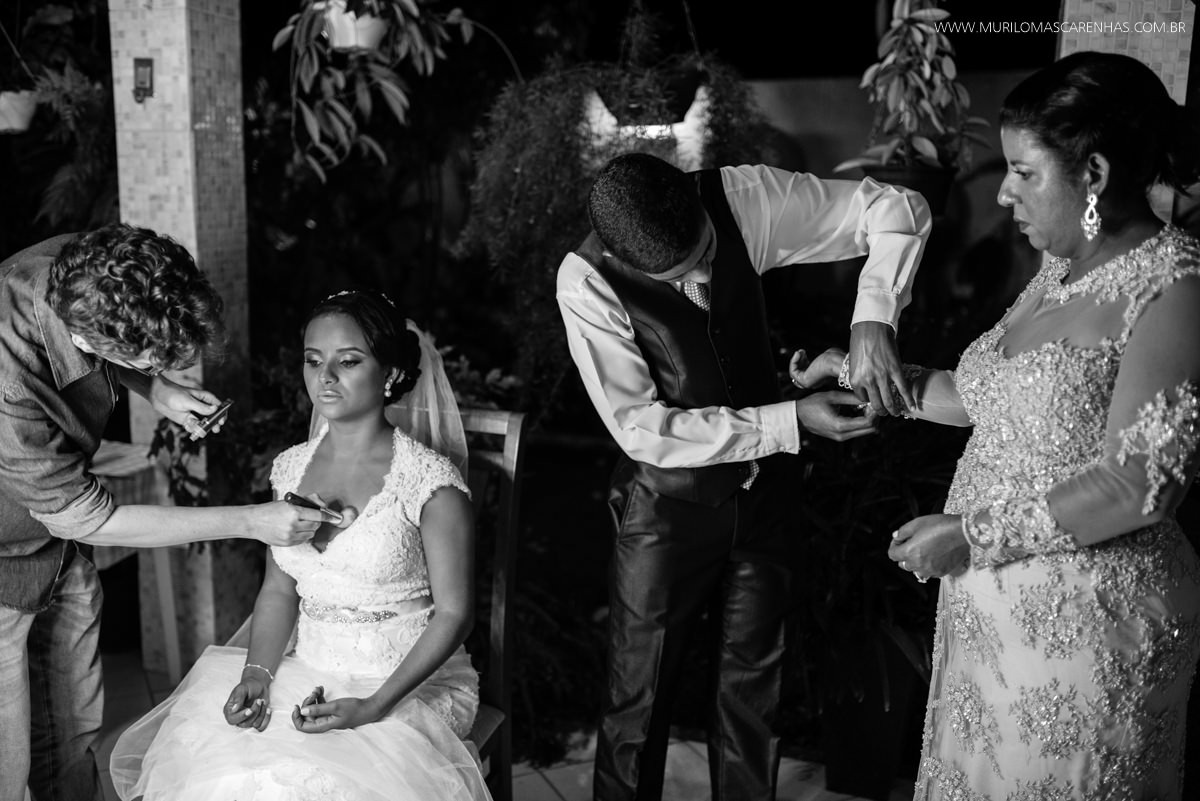 Maquiadora arruma noiva enquanto irmão e mãe se arrumam ao lado